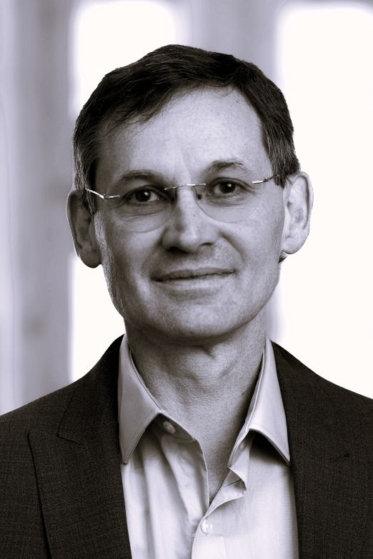 Man wearing a suit jacket and dress shirt against a bright background.